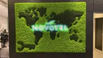Mooswand mit Weltkarte und leuchtendem Novotel-Logo